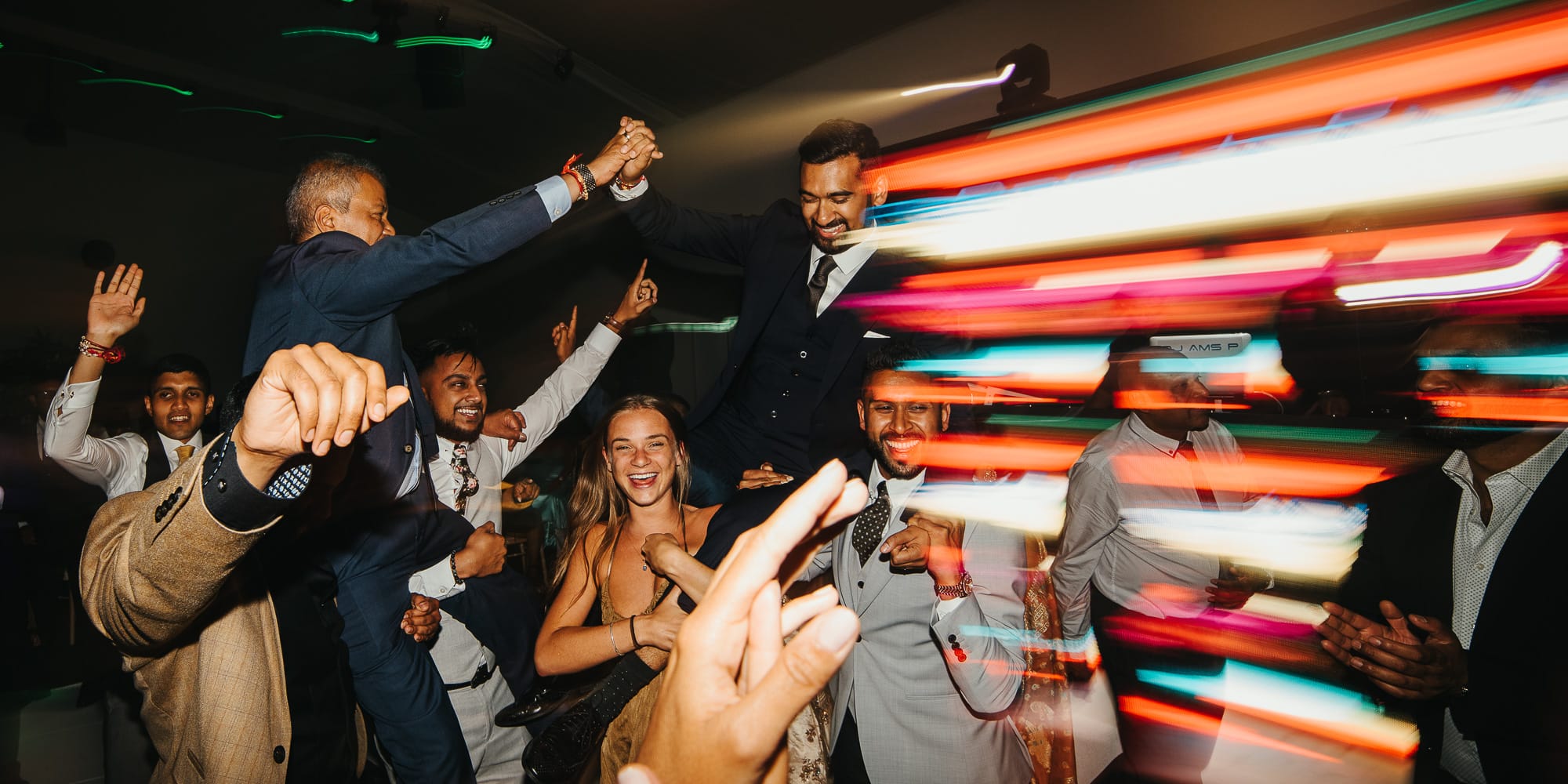 Wedding guests partying on dance floor and holding asian groom on shoulders